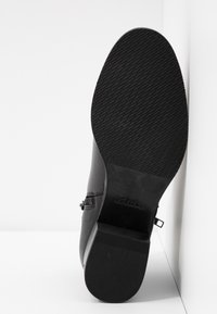 Botín negro hasta el tobillo con un upper de cuero texturizado, tacón bajo en bloque y suela de goma con un patrón de dibujo. Logo de la marca visible en la suela.