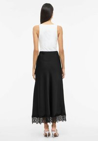 Zwarte satijnen rok met kanten rand aan de zoom, gecombineerd met een wit mouwloos topje. Gladde textuur en vloerbedekkend ontwerp.