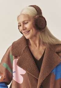 Brązowe nauszniki z polaru z motywem niedźwiedzia, zestawione z kurtką w wielokolorowy kwiatowy wzór w odcieniach brązu, różu i niebieskiego.