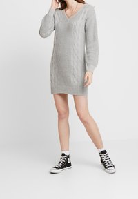 Grå stickad klänning med V-ringning, kabelmönster på sidorna och ribbade ärmslut och fåll, matchad med svarta hög-top sneakers.