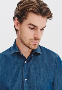 Dżinsowa koszula w ciemnoniebieskim kolorze, z zapięciem na guziki, ostrym kołnierzykiem oraz gładką fakturą z subtelnym blaskiem.