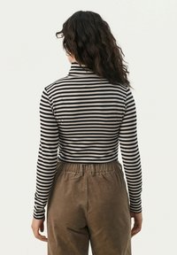 Black and white striped long-sleeve top with a high collar, paired with brown corduroy pants featuring an elastic waistband.