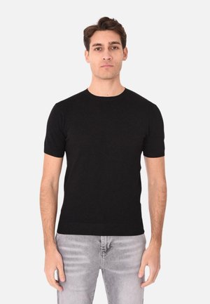 Maglietta nera a maniche corte in maglia con collo rotondo e finiture a coste, abbinata a jeans grigi chiari. Texture liscia, design aderente.