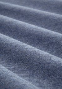 Blått tyg med fin stickning, som visar släta, vågiga linjer och en mjuk yta, vilket framhäver en gradienteffekt från ljusa till mörka nyanser.