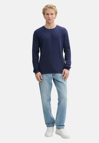 Marineblauw longsleeve shirt met een gestructureerd breipatroon, gecombineerd met lichtblauwe rechte jeans en witte sneakers. Eenvoudige, casual kleding.