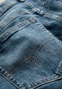 Blå denimtyg med broderad sömnad på ett bakfick. Strukturerat, hållbart material med en slät yta.