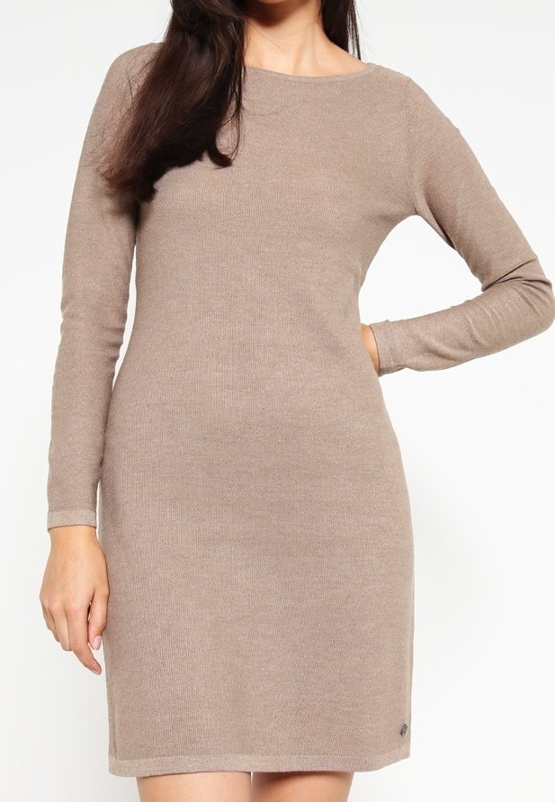 Femme portant une robe en maille beige à manches longues, longueur genou, debout avec une main sur la hanche sur fond blanc uni.