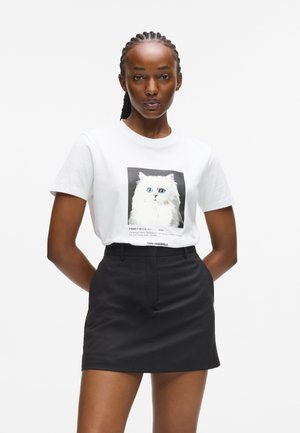 T-shirt en coton blanc avec un graphique de chat noir et blanc, associé à une jupe noire taille haute. Design simple et décontracté.