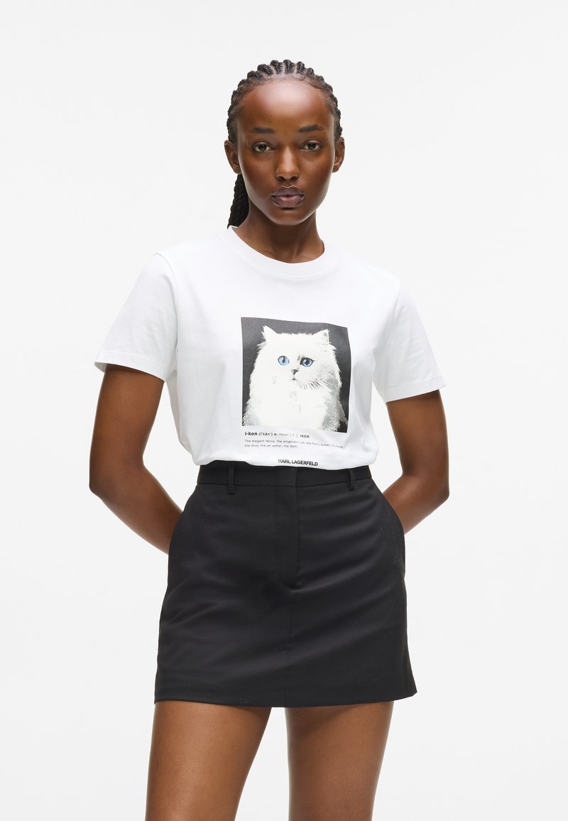 Valge puuvillane t-särk, millel on must-valge kassigraafika, koos musta kõrge vöökohaga seeliku ja lihtsa, mugava disainiga.