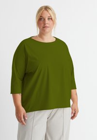 Olivegrünes, oversized Hemd mit rundem Halsausschnitt und Dreiviertelärmeln, aus glattem Stoff gefertigt. Schlichtes Design, ohne Muster oder Akzente.