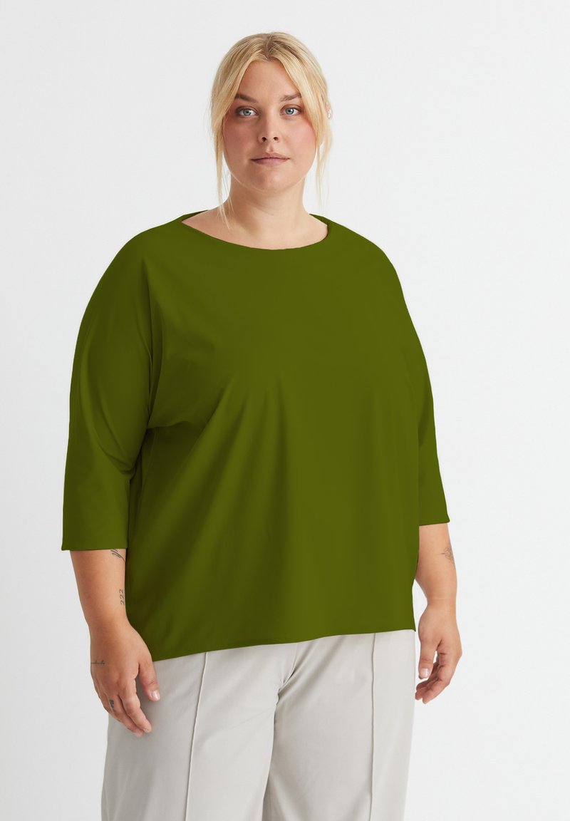 Olivegrünes, oversized Hemd mit rundem Halsausschnitt und Dreiviertelärmeln, aus glattem Stoff gefertigt. Schlichtes Design, ohne Muster oder Akzente.
