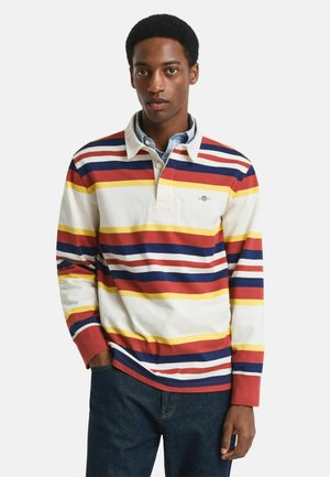 Kopfumfang Langarm-Polohemd mit horizontalen Streifen in Rot, Gelb, Marineblau und Weiß. Mit Kragen und Knopfverschluss, kombiniert mit blauen Jeans.