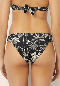 Set de bikini negru cu un model de frunze de palmier în crem. Partea de sus are un spate legat, iar chiloții au o tăietură joasă și o acoperire moderată.