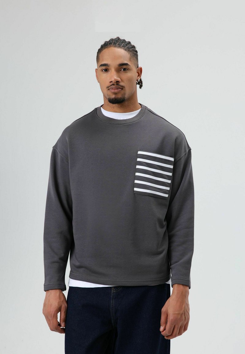 Gray sweatshirt with long sleeves, featuring a white and gray striped pocket. The material is soft, with a relaxed fit and round neckline.