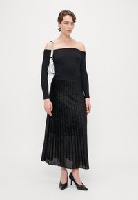 Sort off-shoulder top, plisseret sort nederdel med sølvpynt, parret med sorte højhælede sko og en metallisk sølvtaske.