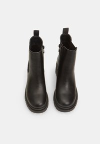 Musta nahkainen nilkkaboots, jossa on sileä pinta, pyöreä varvas, sivuissa vetoketjut ja paksu kumipohja, takana vetoketjut.