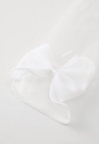 Un nœud en tissu blanc avec une texture lisse, présentant un ruban brillant au centre. Le nœud est légèrement froissé sur un fond clair.