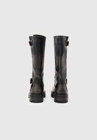 Botas de cuero negro hasta la rodilla con un acabado envejecido, que presentan doble hebilla, suela de goma resistente y costuras reforzadas.
