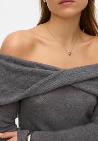 Szary sweter odsłaniający ramiona z prążkowaną fakturą i skrzyżowanym detalem z tkaniny, zestawiony z delikatnym srebrnym naszyjnikiem z małym wisiorkiem.