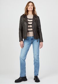 Musta nahka-motoristineule, beige ja musta raidallinen neulepaita, vaaleansiniset farkut ja mustat paksupohjaiset saappaat. Malli seisoo suorassa.