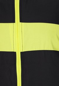 Vysoce viditelná bunda s reflexními žlutými pruhy na černém pozadí. Má přední zip a texturovanou tkaninu.