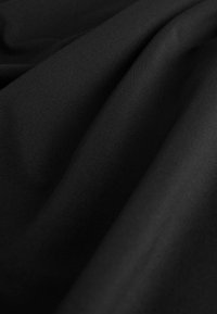 Czarny materiał o fakturowanej, prążkowanej powierzchni, ukazujący gładkie układanie i jednolitą głębię koloru. Brak widocznych wzorów lub akcentów.