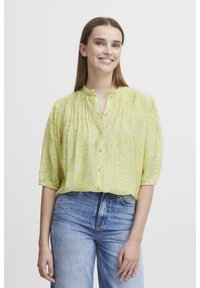 Blusa a maniche corte con bottoni di colore verde chiaro, con motivo astratto bianco. Presenta un colletto alla cinese e una vestibilità rilassata. Realizzata in tessuto leggero.