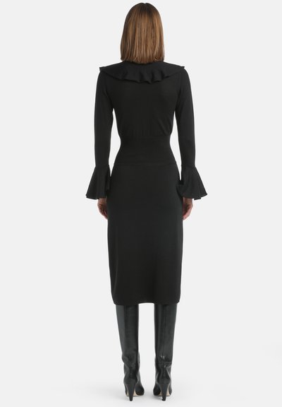 Czarna, długozwałkowa sukienka dzianinowa z falbaniastym kołnierzem i rozszerzanymi mankietami, dopasowana w talii, z prostą, midi długością spódnicy; noszona z czarnymi kozakiem za kolano.