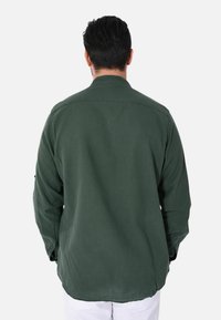 Camicia verde a maniche lunghe con colletto, polsini a bottoni e vestibilità comoda. Texture liscia, realizzata in cotone o materiale simile.