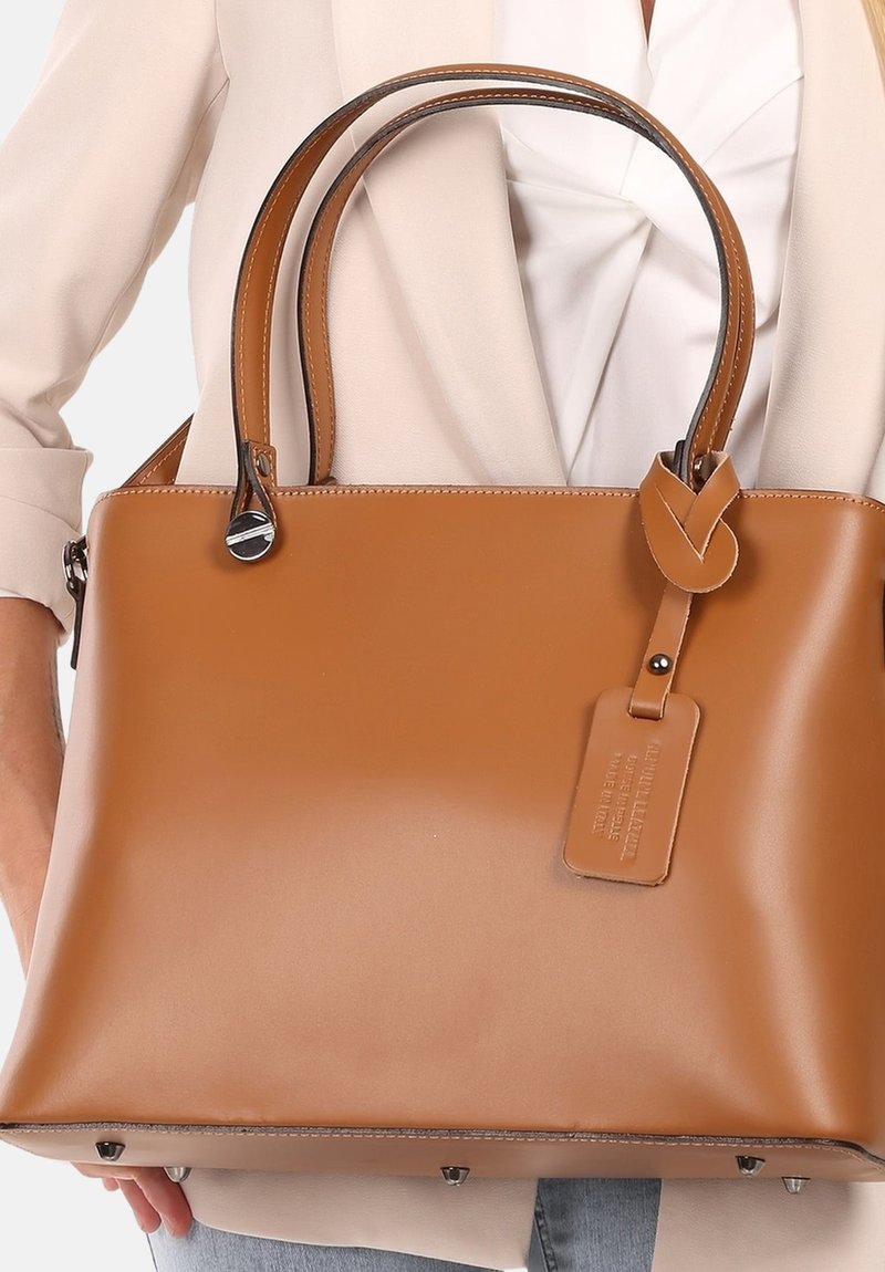 Bruine leren handtas met een gestructureerde vorm, dubbele handvatten, subtiele glanzende afwerking en een afneembare tag. Bevat zilverkleurige hardware aan de onderkant.