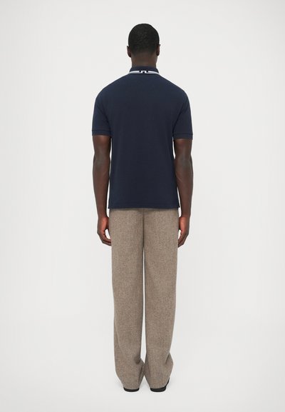 Námornícka polokošeľa s bielym golierom, v kombinácii so svetlohnedými nohavicami s širokými nohami. Tkanina pôsobí hladko a upravene.