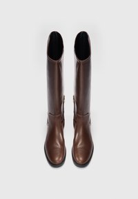 Botas de cuero marrón hasta la rodilla con una textura suave, puntera redondeada, silueta esbelta y detalle de cremallera dorada en el costado.
