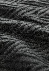 Grau gestrickter Stoff mit einem strukturierten Zickzackmuster, das eine weiche Oberfläche und verschiedene Grautöne zeigt.