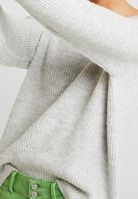 Hellgrau gestrickter Pullover mit lockerer Passform, ausgestattet mit weitem Rippenmuster und gesenkten Schultern, kombiniert mit grünen hochtaillierten Hosen.