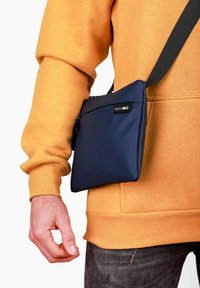 Tmavě modrá kabelka přes rameno s hladkou texturou, nastavitelným popruhem a přední kapsou; na boku s logem VUCH.