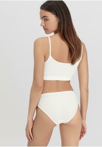 Witte katoenen bralette en hooggekraagde slip met een naadloos design, dunne bandjes en een zachte textuur. Achteraan is er minimale bedekking.