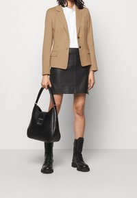 Blazer marrone, blusa bianca, gonna di pelle nera, grande borsa nera con logo, e stivali da combattimento neri con lacci. Texture lisce e design su misura.
