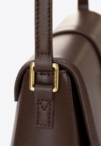 Borsa a tracolla in pelle marrone con una forma strutturata, caratterizzata da dettagli hardware dorati e cuciture visibili sulla tracolla e sul corpo.