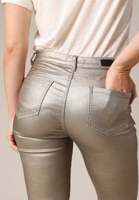 Metalen gouden skinny jeans met een hoge taille, voorzien van achterzakken en een gladde, glanzende textuur. Draag een lichtgekleurde, casual t-shirt.