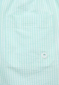 Světle modrá pruhovaná tkanina se čtvercovou kapsou. Kapsa má bílé švy a kovový okraj v pravém dolním rohu.