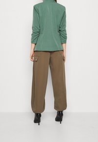 Grön skräddarsydd jacka med trekvartslånga ärmar, kombinerad med lösa bruna cargobyxor med sidofickor och svarta högklackade stövlar.