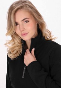 Maglione in fleece nero con zip e colletto alto, caratterizzato da una texture liscia e una chiusura con zip frontale. Accentato da un branding sottile sulla manica.