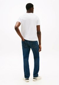 Hvid kortærmet t-shirt, blå denim jeans og hvide sneakers set fra ryggen. Jeansene har baglommer og en lige pasform.