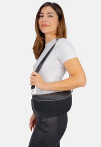 Schwarze Leder-Umhängetasche mit runder Form, Reißverschluss und abnehmbarem Tragegurt. Die Textur wirkt genoppt und zeigt Langlebigkeit.