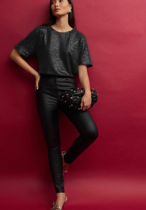 Zwart paillettentop met korte mouwen, gecombineerd met hoge zwarte lerenachtige broek en een gestructureerde zwarte clutch met metalen accenten.
