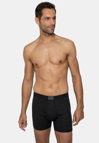 Schwarze Baumwollboxershorts mit gerippter Textur und elastischem Bund, der ein Etikett präsentiert. Die Shorts sind körpernah geschnitten und haben eine Länge bis zur Mitte des Oberschenkels.