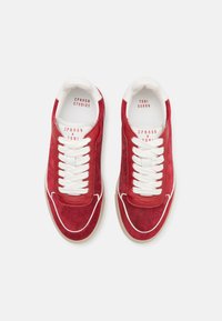 Sneaker in suede rosso con lacci bianchi, dotati di una linguetta in pelle liscia e suola in gomma beige. Gli accenti includono cuciture bianche e branding.