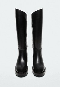 Bottes noires montant jusqu'au genou en cuir lisse, avec un bout arrondi et une semelle épaisse noire. Design élégant avec un minimum de détails et d'accents.
