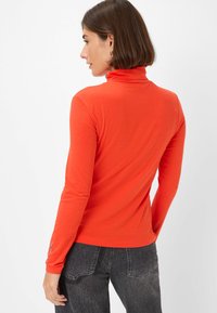Langsleeve turtleneck in fel oranje, gemaakt van gladde stof, met een aansluitend ontwerp en elegante lijnen. De achterzijde toont minimale details.