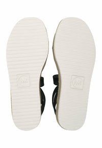 Para czarnych sandałów pokazana z białych, żłobionych podeszw z tłoczonym logo MK w pobliżu pięty i osłoniętymi jute'owym brzegami platformy.